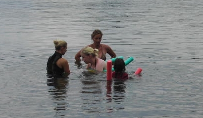 Eine junge Frau schwimmt mit Hilfe von 2 Therapeutinnen im See